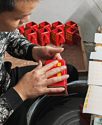 Worker applying decals to ceramic mugs at Haohan Ceramics Factory - Form Feast